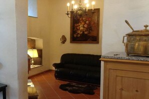 A living room with a black leather sofa, a chandelier, a painting, and a stove.