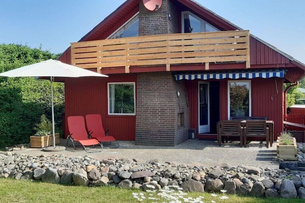 Een rood gebouw met een bakstenen schoorsteen, een houten terras en een patio met twee rode stoelen en een tafel.