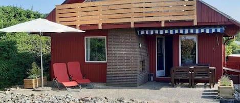 A red building with a brick chimney, a wooden deck, and a patio area with two red chairs and a table.