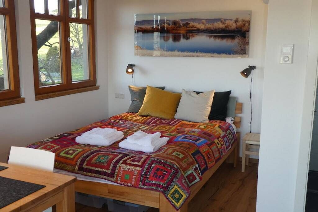 A bedroom with a bed, a painting, a window, and a bedside table.