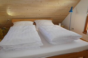 Un letto singolo con biancheria da letto bianca in una stanza con travi in legno al soffitto.