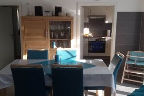 Un coin repas avec une table et des chaises, une cuisine en arrière-plan et un meuble avec des portes en verre.