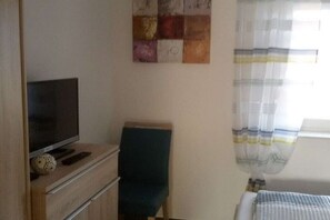 Une pièce avec un téléviseur posé sur un meuble en bois, une chaise et un lit agrémenté d’un rideau à rayures.