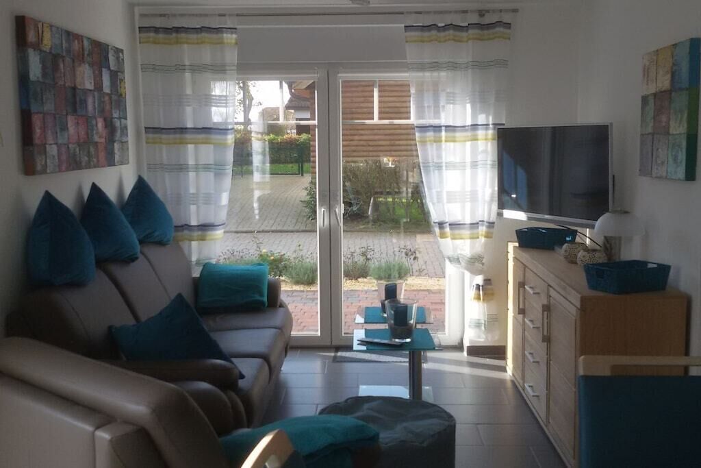 A living room with a sofa, television, and a view through a glass door to the outside.