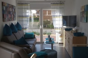 A living room with a sofa, television, and a view through a glass door to the outside. - Villa Belair Schmidt (Wurster Nordseeküste Ortsteil Dorum-Neufeld)