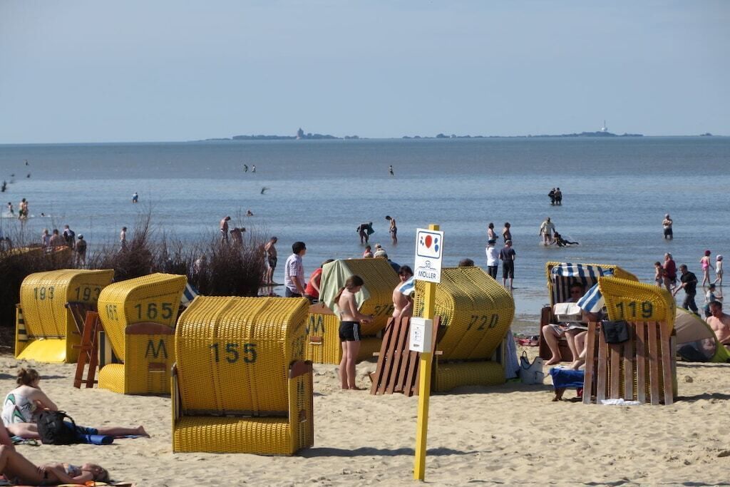 A beach with yellow chairs marked with numbers, a sign indicating a lifeguard area, and people swimming in the water.