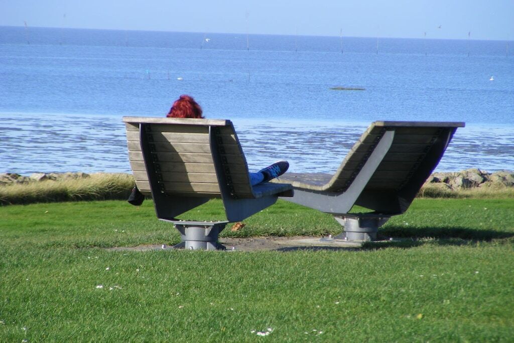 En bänk där en person sitter och blickar ut över en vattenyta.