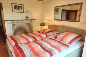 Un dormitori amb un llit, una taula de nit, una làmpada, un radiador, un mirall i una fotografia emmarcada a la paret.