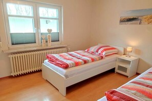 Ein Einzelzimmer mit Heizkörper, Nachttisch inklusive Lampe und einem Fenster mit Jalousien.