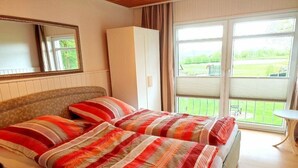 Un lit double avec une literie à rayures, une armoire, un miroir et un balcon avec vue.