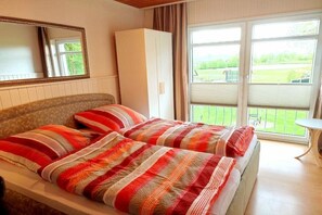 Un lit double avec une literie à rayures, une armoire, un miroir et un balcon avec vue.