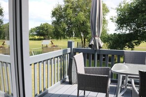 Une terrasse dotée de meubles en osier et d’une table, donnant sur un espace verdoyant bordé d’arbres.