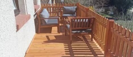 A wooden deck with outdoor furniture, a wooden fence, and a building in the background.
