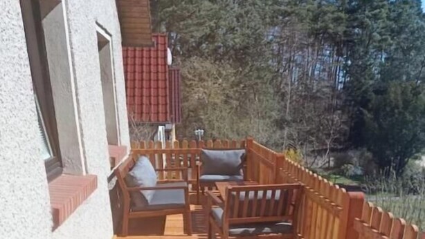 Un patio in legno con mobili da esterno, una recinzione di legno e un edificio sullo sfondo.