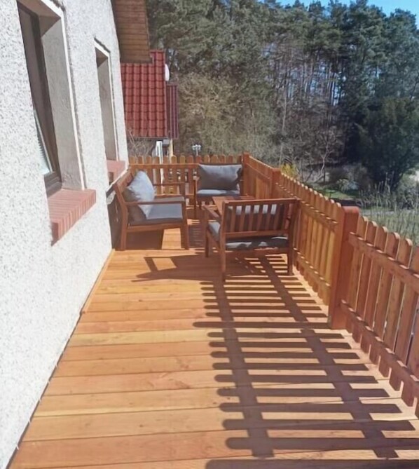 Een houten terras met buitenmeubilair, een houten schutting en een gebouw op de achtergrond.