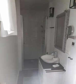 Een badkamer met een wit wastafel, een spiegel en een douche.