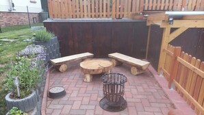 Patio esterno con tavolo e panche in legno, circondato da pavimento in mattoni e recinzione in legno.
