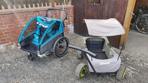 Una carrozzina con tenda parasole e un triciclo con tenda parasole, parcheggiati su una superficie in pietra.