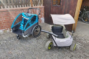 Een kinderwagen met kap en een driewieler met kap, geparkeerd op een geplaveid oppervlak.