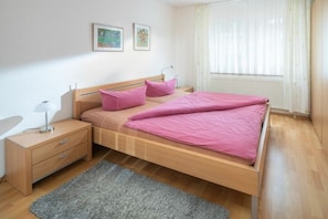 A bedroom with a wooden bed, a nightstand, a lamp, and a window with curtains. - Holiday apartment in Juist with swimming pool (Juist)