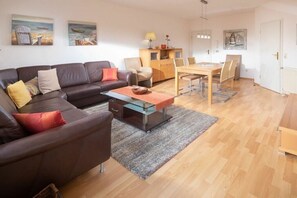 Uma sala de estar com sofá de couro marrom, mesa de centro de vidro e área de jantar com mesa e cadeiras de madeira.