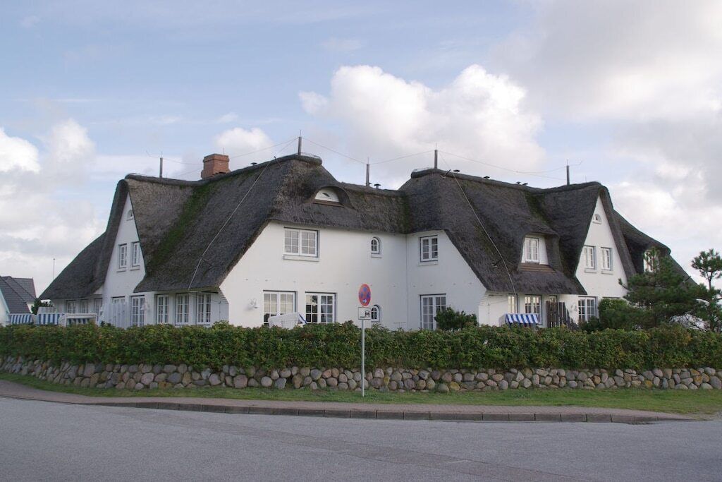 A white building with a unique thatched roof design, a stone wall in front, and a clear sky.