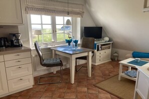 A compact kitchen with a dining area, a television, and a view of the outdoors. - "Dream view" in the Sölring-Hüs (Sylt\/OT Rantum)