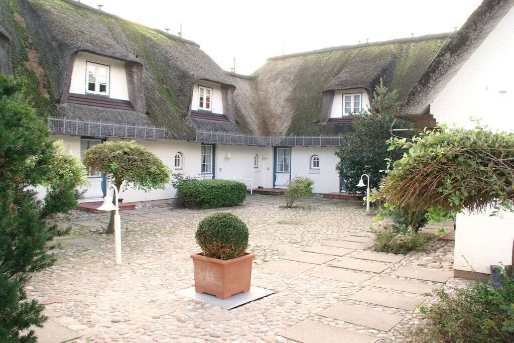 A courtyard with thatched-roof buildings, stone paving, and potted plants.
