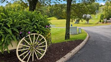 A paved road curving through a landscaped area with a large wooden wheel planter filled with greenery and flowers.