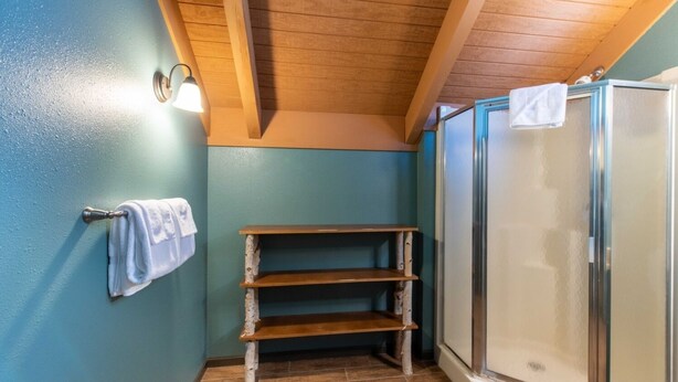 A bathroom with a wooden shelf, a towel rack, and a glass shower enclosure.