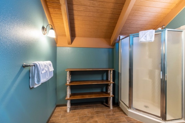 A bathroom with a wooden shelf, a towel rack, and a glass shower enclosure.