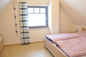 A bedroom with a window, a bed with a checkered bedspread, and a curtain. - Holiday home in Glowe with swimming pool (Glowe)