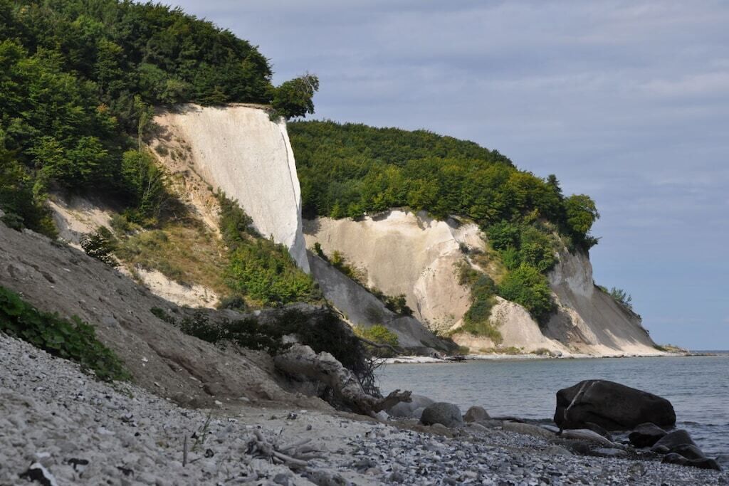 Een kustlandschap met een hoge klif, een kiezelstrand en een wateroppervlak.