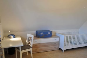 A room with a white crib, a desk with a chair, and a blue suitcase on a dresser. - Holiday home in Glowe with swimming pool (Glowe)