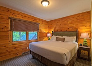 Ein Zimmer mit Holzwänden, einem Bett, zwei Nachttischlampen und einem Fenster mit Jalousien.