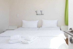 A double bed with white linens and two pillows, a bedside table, and a wall-mounted light fixture. - "Waterkant" at Uns to Hus (Juist)