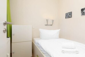 A single bed with white bedding, a green curtain, a wall-mounted light fixture, and a small framed picture. - "Waterkant" at Uns to Hus (Juist)
