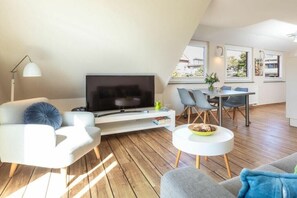 A modern living room with a flat-screen TV, a sofa, a coffee table, and a dining area with chairs and a table. - "Waterkant" at Uns to Hus (Juist)
