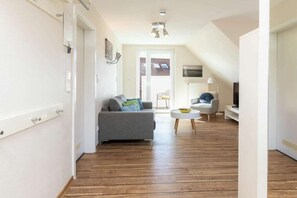 A modern living room with a grey sofa, a white coffee table, and a television on a stand. - "Waterkant" at Uns to Hus (Juist)