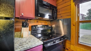 Una cocina compacta con estufa de acero inoxidable, microondas y armarios de madera.