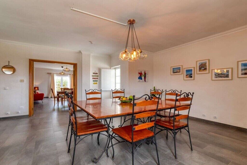 A dining area with a wooden table and chairs, a hanging light fixture, and framed pictures on the wall.
