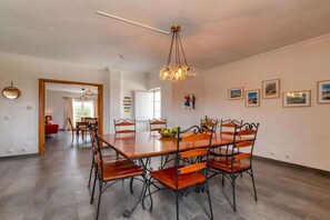 A dining area with a wooden table and chairs, a hanging light fixture, and framed pictures on the wall. - Villa in Ribamar with swimming pool (Ribamar)