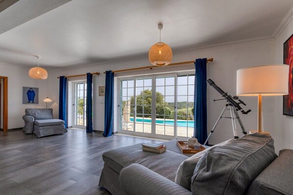 A spacious living room with a large window, a telescope, and a pool view.