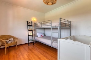 A bunk bed room with a wooden floor, a wicker chair, and a white crib.
