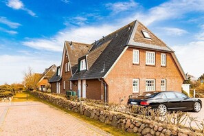 A row of brick houses with pitched roofs, a stone wall, and a parked car. - Cozy "Wadden Sea gem" with south-facing terrace (Munkmarsch)