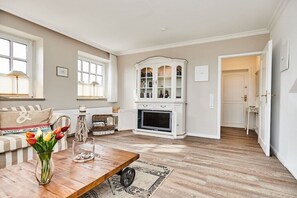 A living room with a wooden coffee table, a vase with flowers, a fireplace, and a white cabinet. - Cozy "Wadden Sea gem" with south-facing terrace (Munkmarsch)