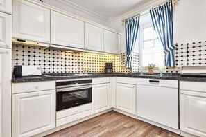 A modern kitchen with white cabinetry, a black and white patterned backsplash, a built-in oven, and a dishwasher. - Cozy "Wadden Sea gem" with south-facing terrace (Munkmarsch)