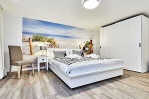A bedroom with a large bed, a chair, a bedside table, and a wardrobe. - Cozy "Wadden Sea gem" with south-facing terrace (Munkmarsch)