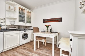 Cozinha com armários brancos, máquina de lavar, mesa de jantar com cadeiras e um objeto decorativo na parede.