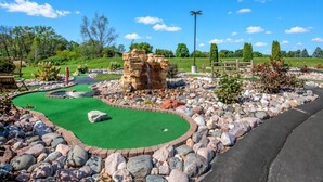 Un parcours de minigolf avec un tapis vert pour les putts, un obstacle constitué d’une formation rocheuse et une clôture en bois en arrière-plan.